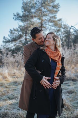Familienfotografie: Schwangeres Paar steht im Freien und hält gemeinsam den Babybauch, ruhige Aufnahme nahe Hohenkammer.