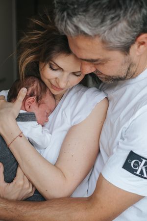 Neugeborenenfotografie: Eltern halten ihr Baby eng bei sich und blicken ruhig auf das schlafende Kind.