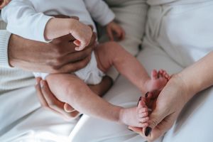 Babyfotografie: Detailaufnahme der Füße eines Neugeborenen, gehalten von den Händen der Eltern im weichen Licht.