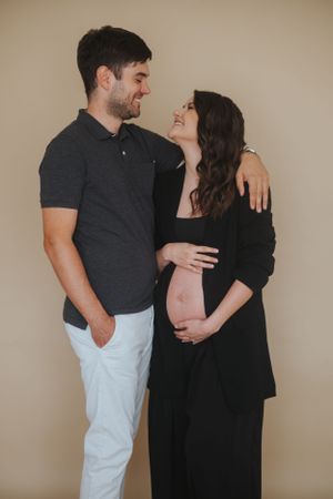 Familienfotografie: Schwangeres Paar steht sich im Studio gegenüber, natürliche Aufnahme mit Fokus auf Nähe.