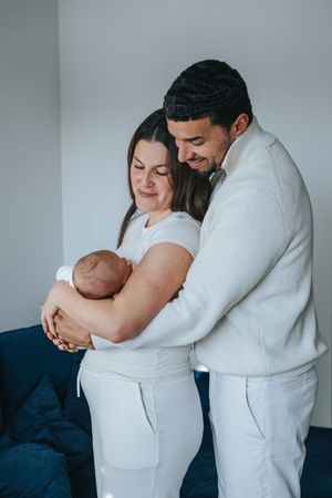 Familienfotografie: Eltern stehen eng beieinander und halten ihr Baby, natürliche Aufnahme im Alltag.“