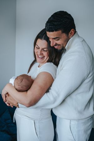 Familienfotografie: Eltern halten ihr Neugeborenes im Arm, ruhiger Moment der Nähe im hellen Raum.