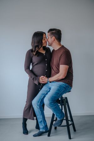 Familienfotografie: Die werdenden Eltern sitzen auf einem Hocker im Studio und blickt sich ruhig an.