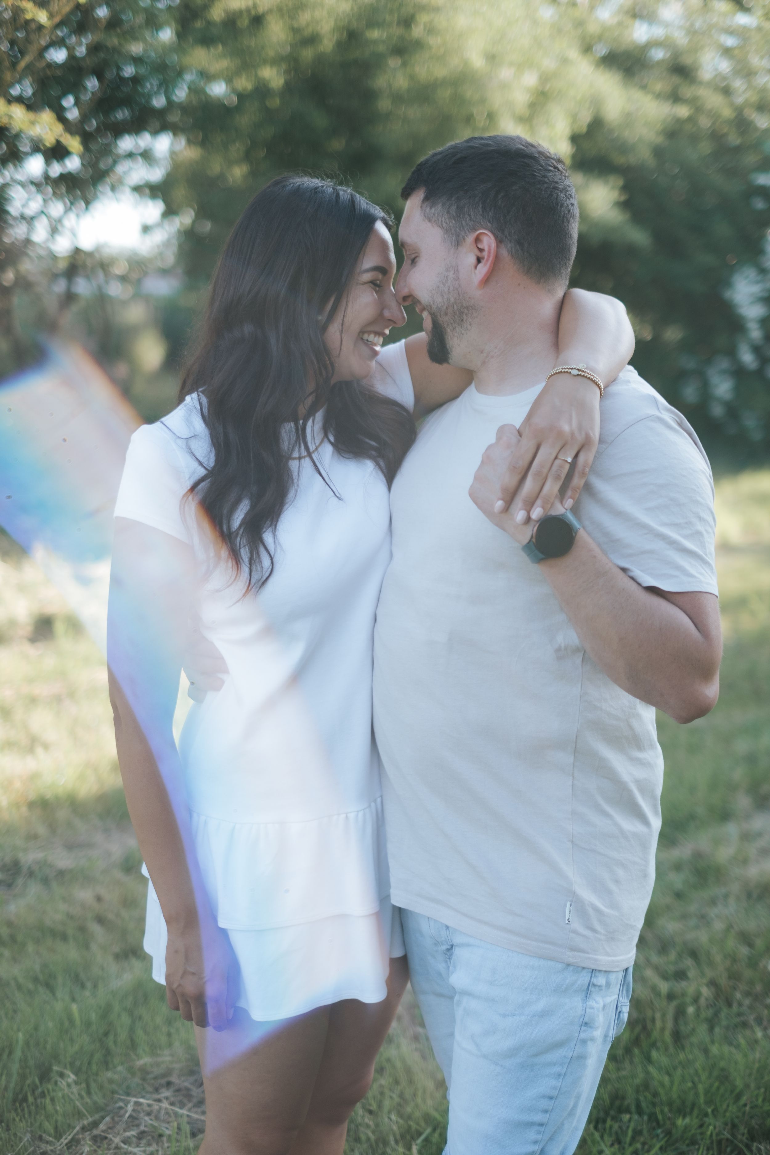 Paarfotografie: Fotografie eines Paares im Grünen, eng umarmt und lächelnd, aufgenommen im natürlichen Licht beim Verlobungs-Fotoshooting.
