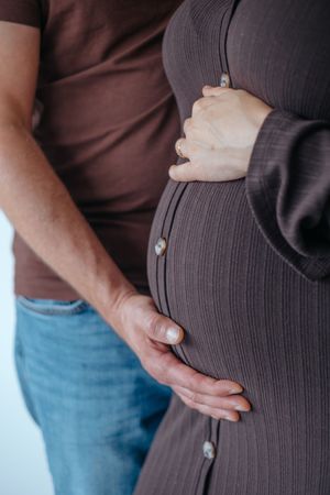 Familienfotografie: Detailaufnahme eines Babybauchs, die Hände eines Paares liegen schützend darauf.