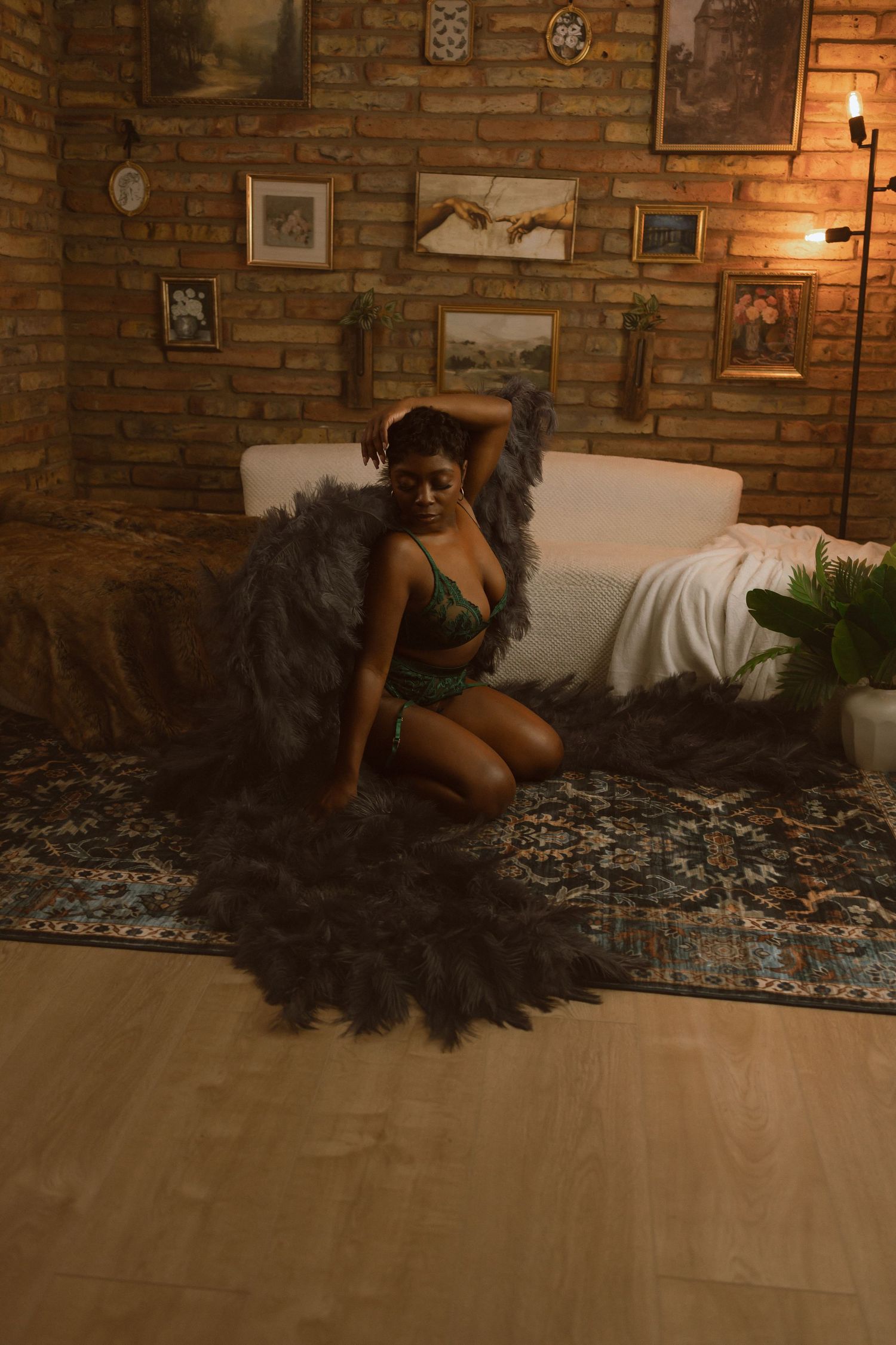 A figure in a black tulle dress poses gracefully on a hardwood floor against exposed brick walls in warm lighting.