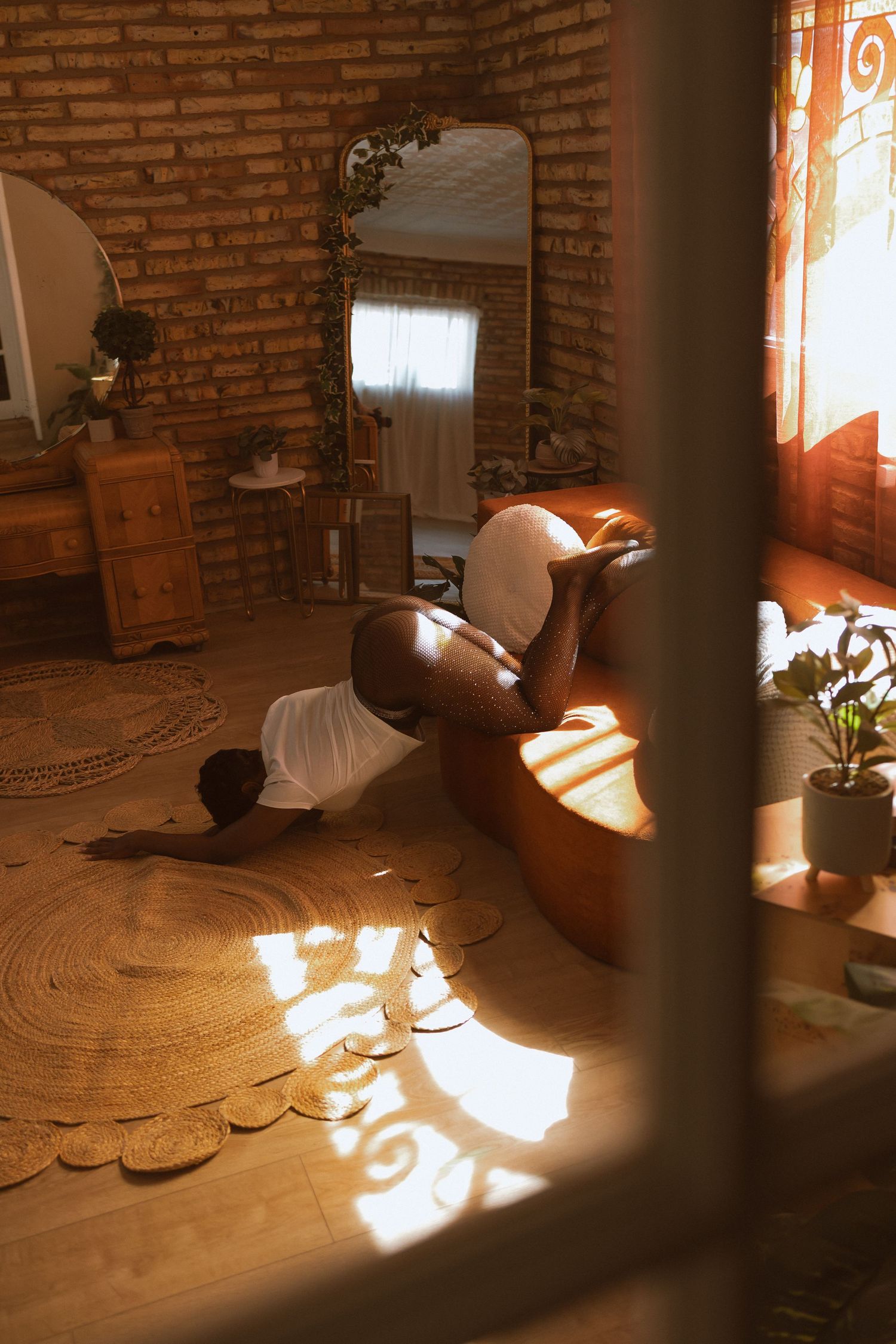 Warm sunlight streams through window onto wooden floor in cozy room with exposed brick wall and decorative mirror.