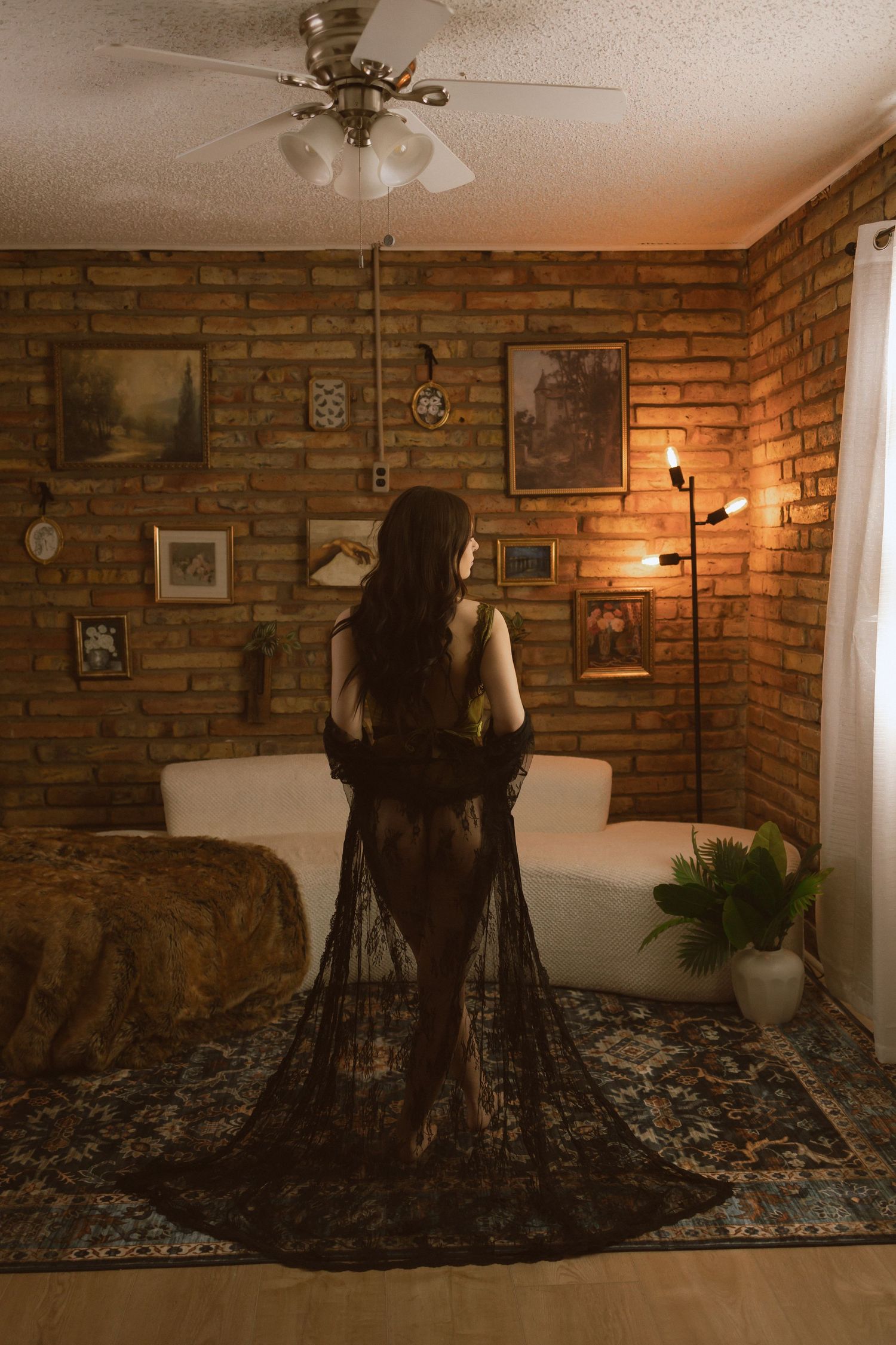 A black lace dress photographed against exposed brick walls in a dimly lit room with vintage decor and wall art.