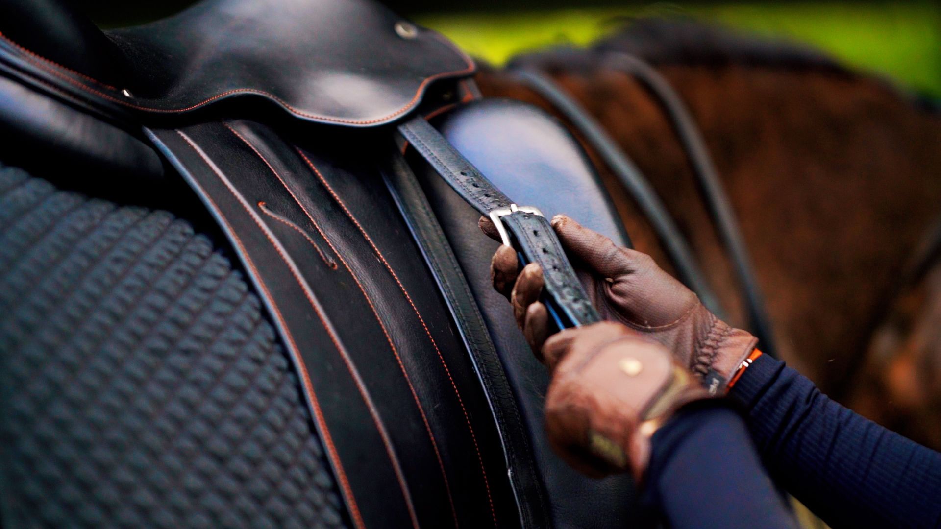 Close-up of hands adjusting black leather saddle straps and buckles.