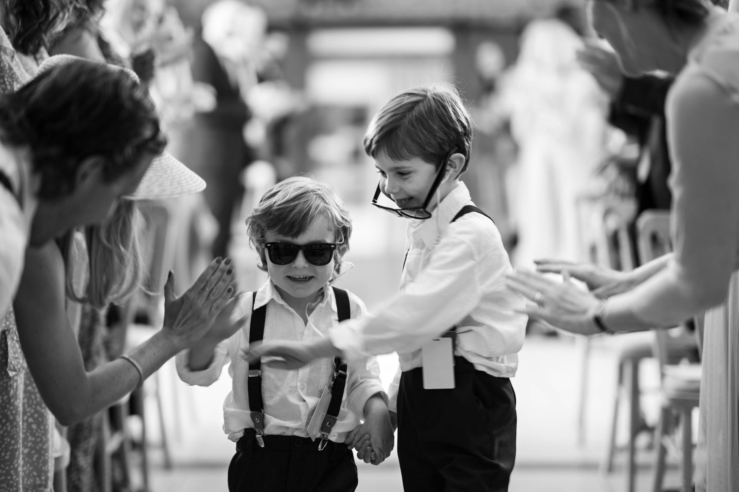 Two young children in formal attire with suspenders dance together at what appears to be a wedding or celebration.