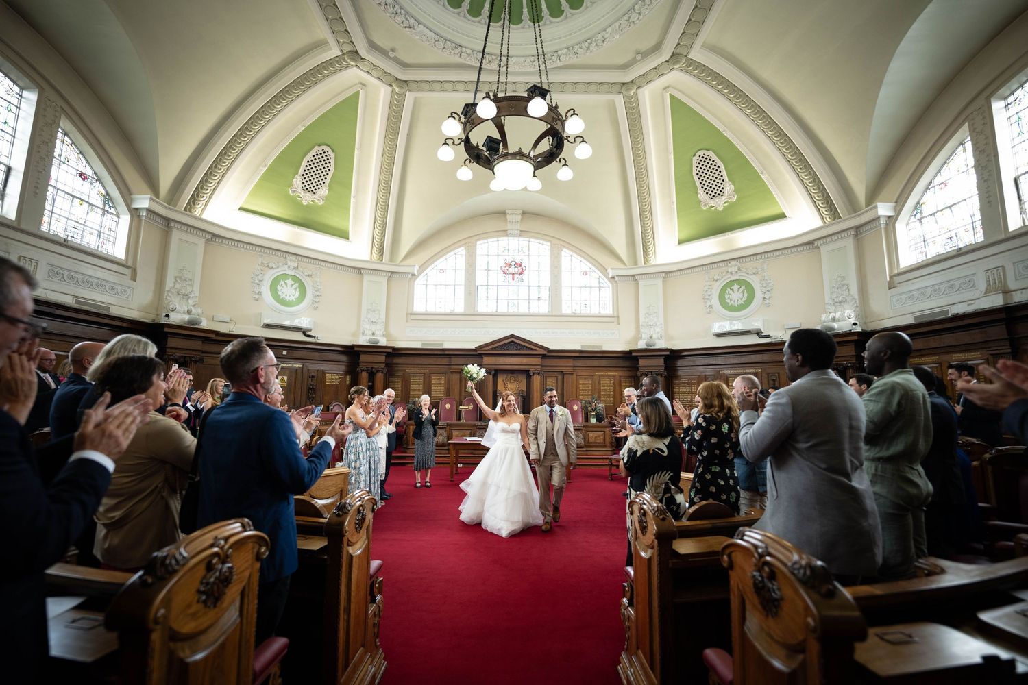 Interior wedding ceremony in a historic chapel with vaulted ceiling, ornate architecture and guests seated in wooden pews.