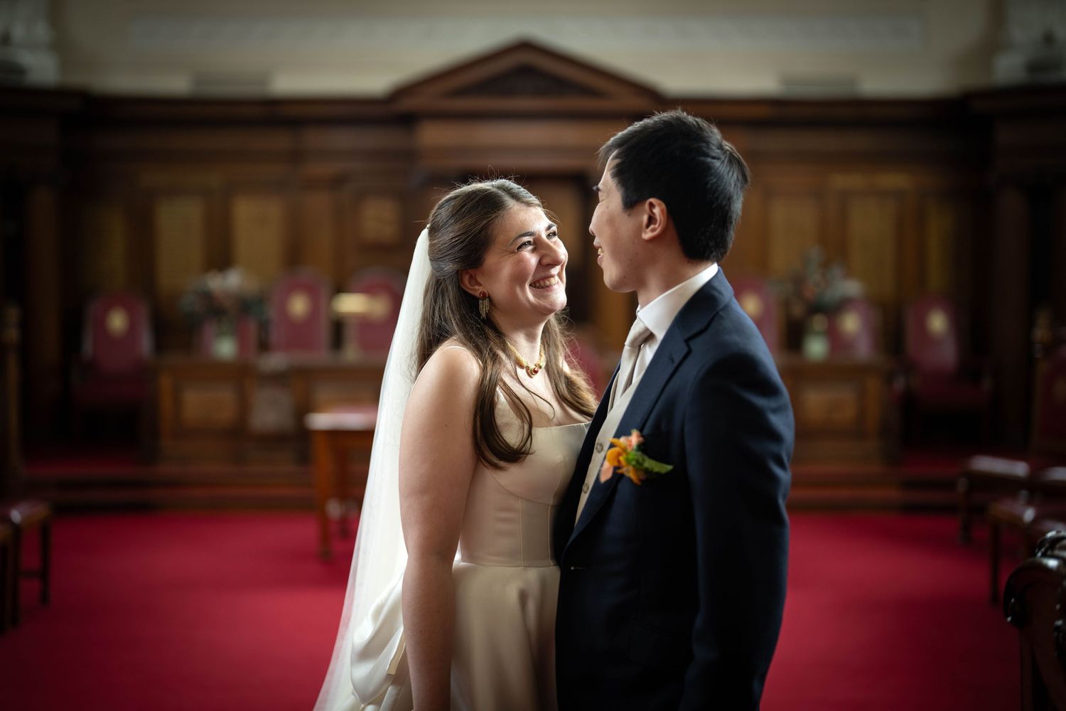 Couple shares a tender moment on their wedding day inside a church with wooden panels and red carpet.