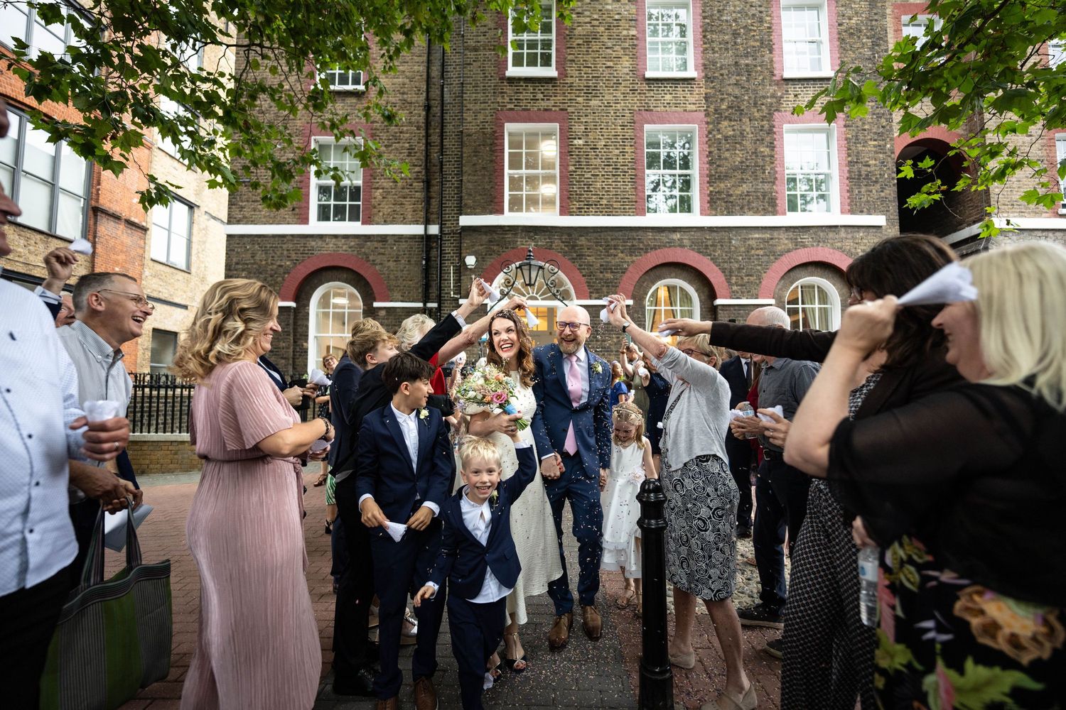 Wedding guests celebrate outdoors in a courtyard surrounded by brick buildings.