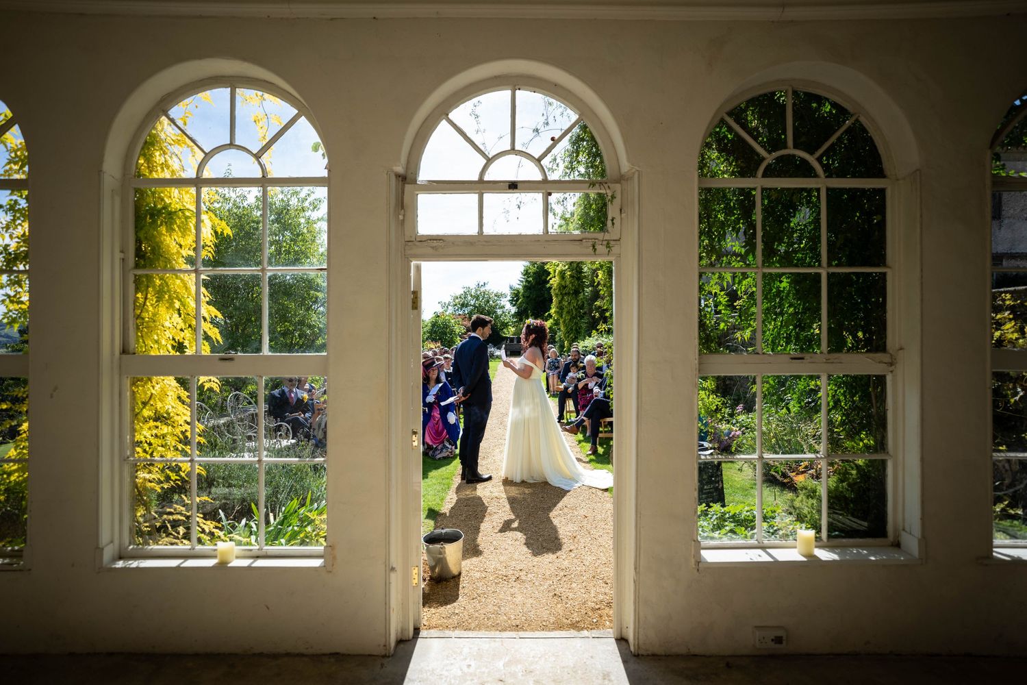 Silhouette of wedding couple framed by arched windows overlooking a garden.