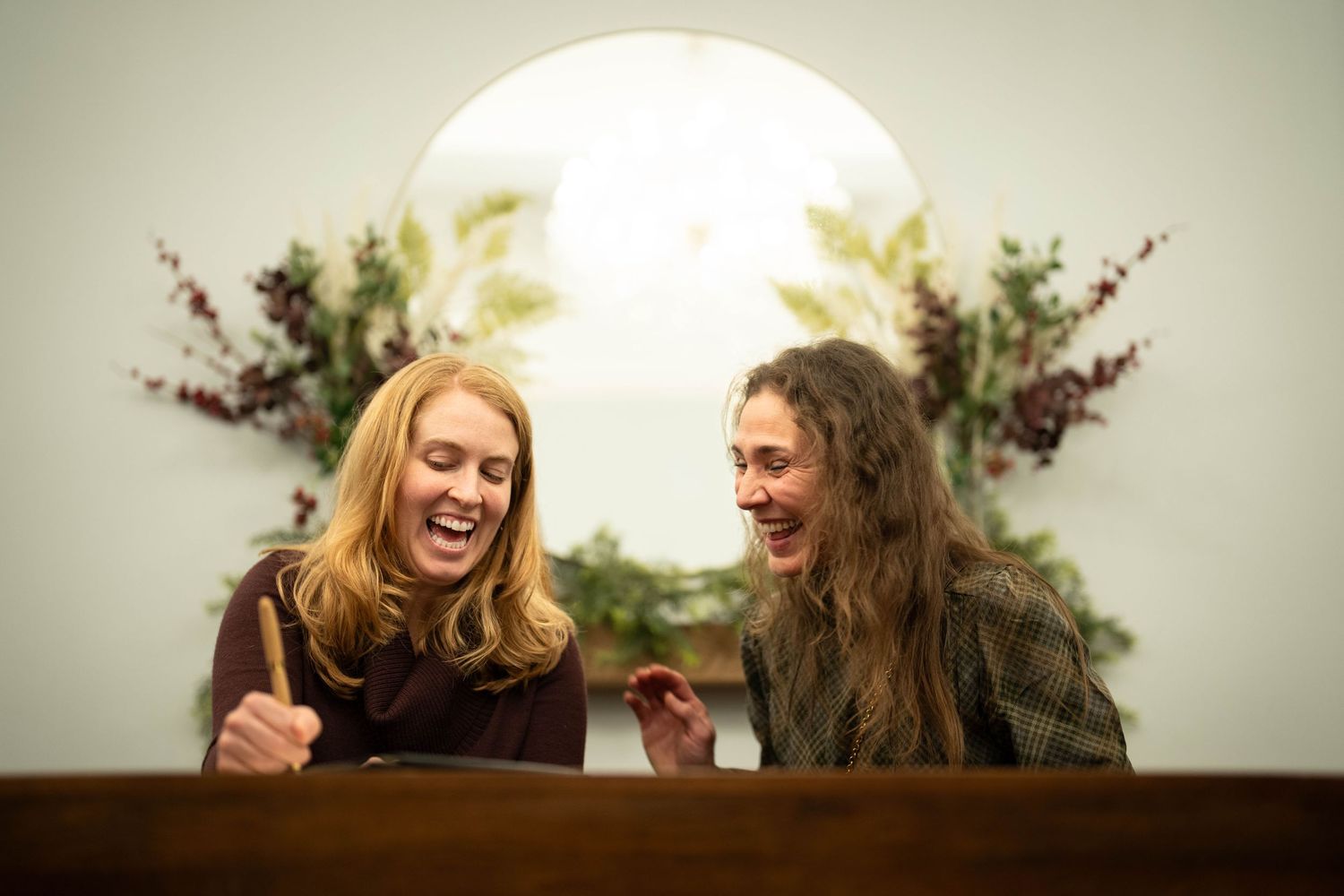 Two friends sharing a laugh while sitting together in a warmly lit room.