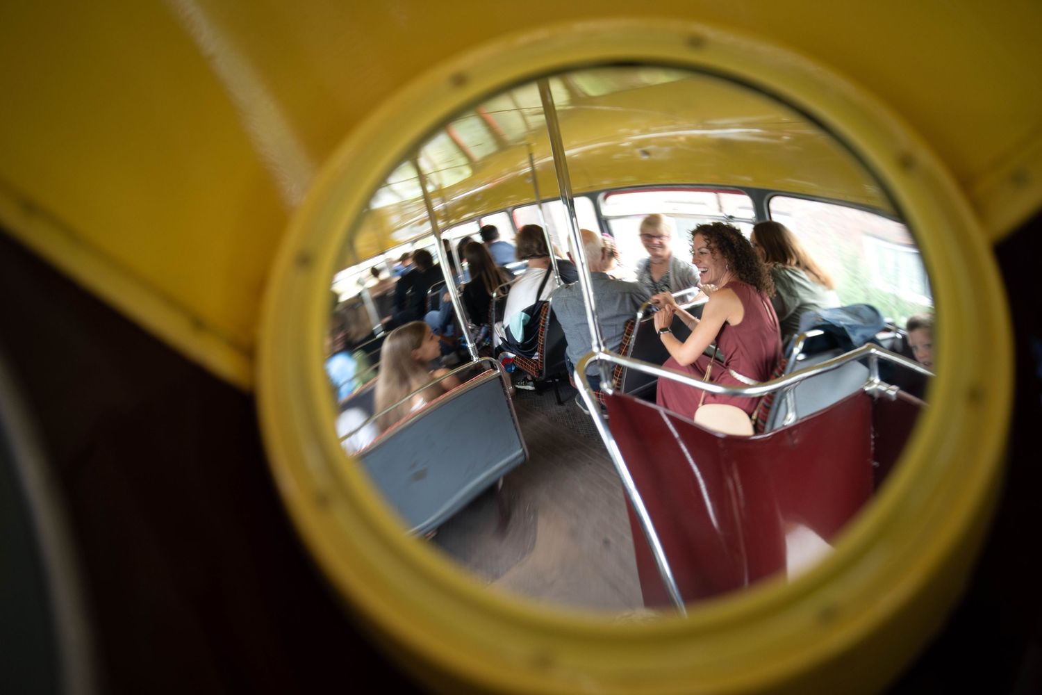 Circular side mirror reflection showing passengers seated inside a crowded bus or transportation vehicle.