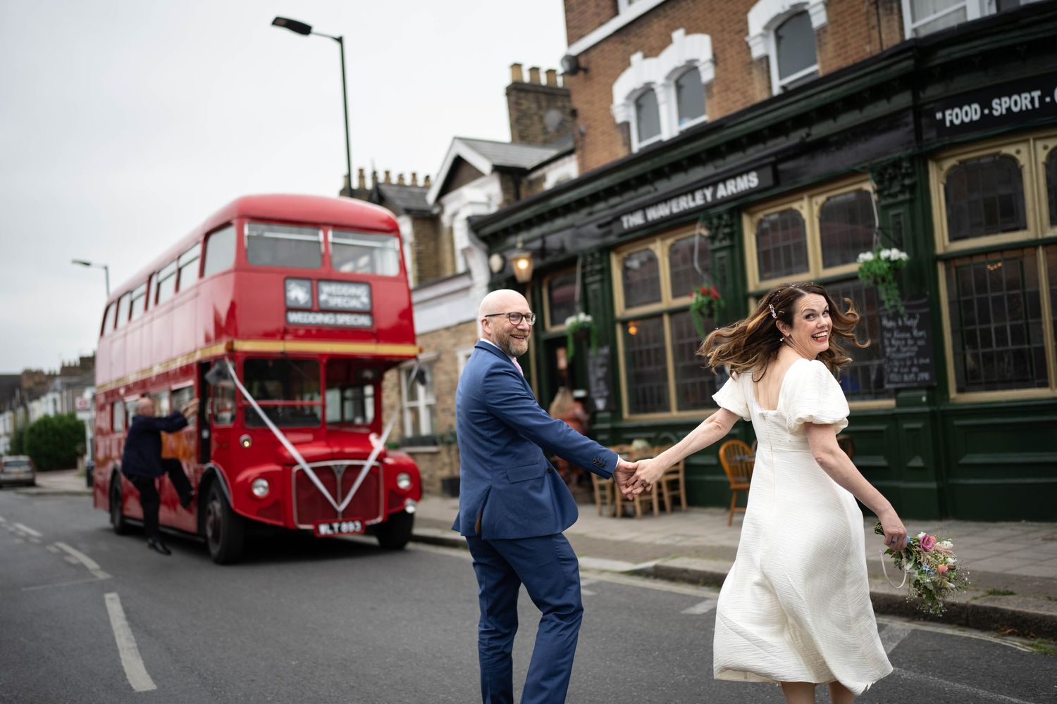 A couple dances joyfully in the street with a vintage red double decker London bus in the background.