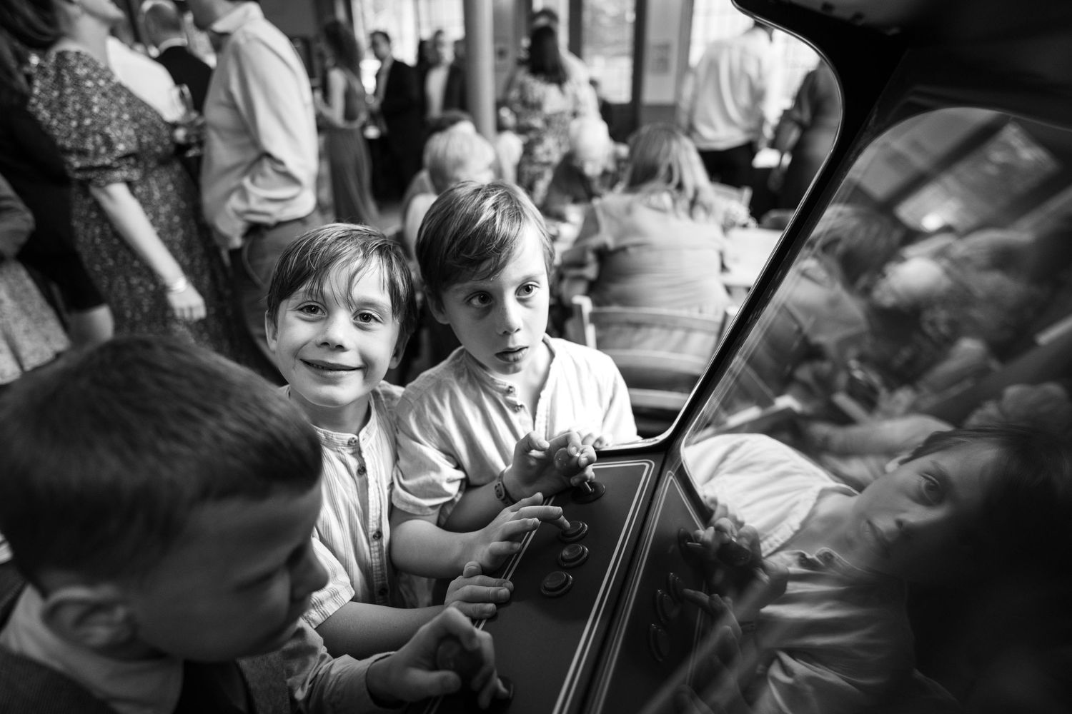 Black and white photograph of children gathered around a piano in a crowded space with joyful expressions.