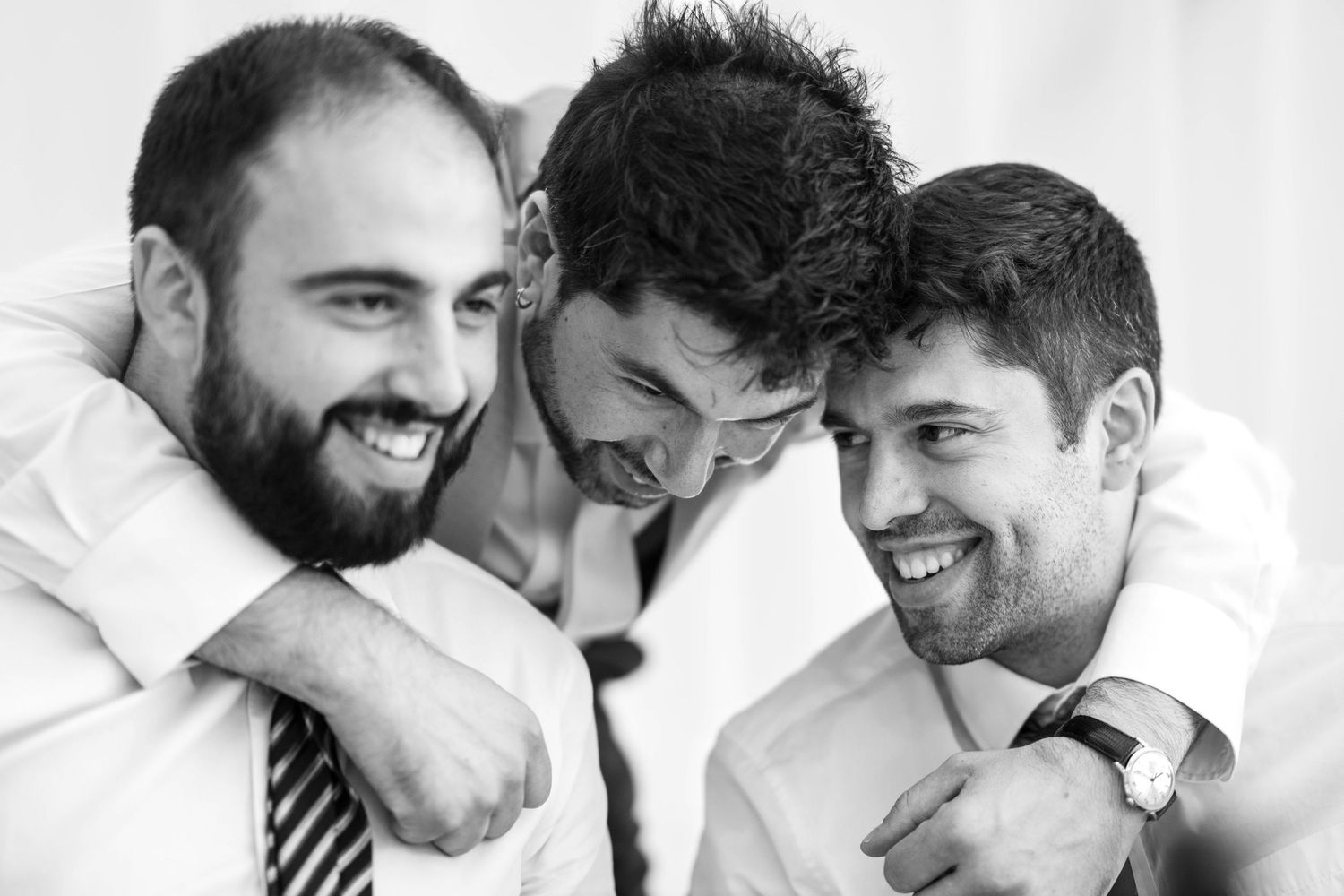 Three joyful friends in formal attire share a candid black and white moment together while laughing.