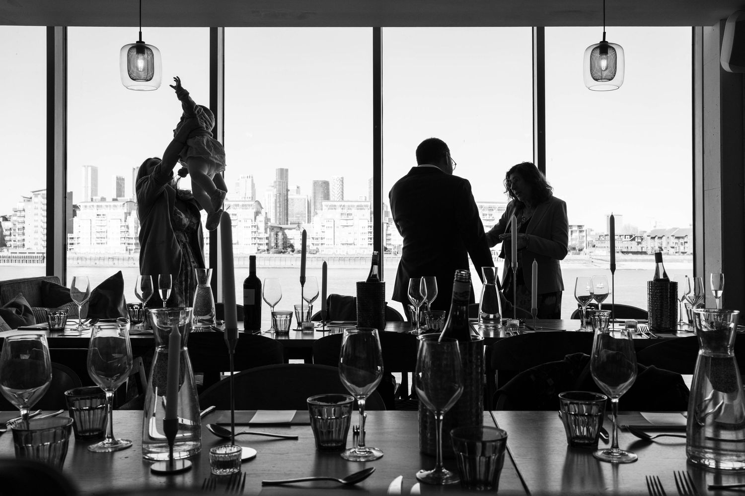 Silhouettes of people exercising on stationary bikes in a gym with city skyline views through large windows.