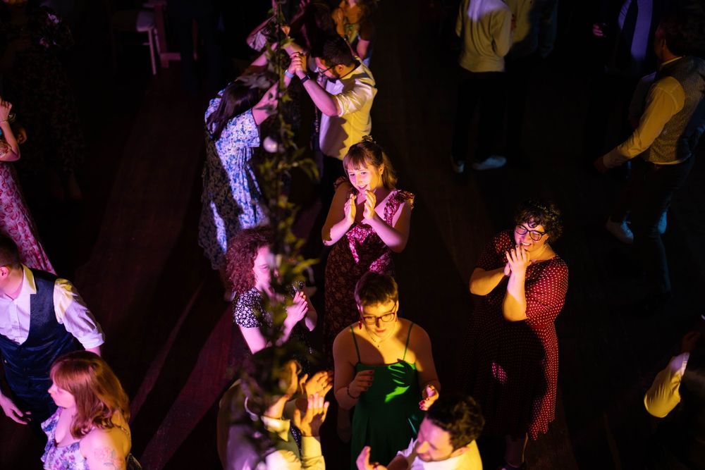 Crowd of people dancing under colorful purple and yellow lights at a nightclub or party venue.