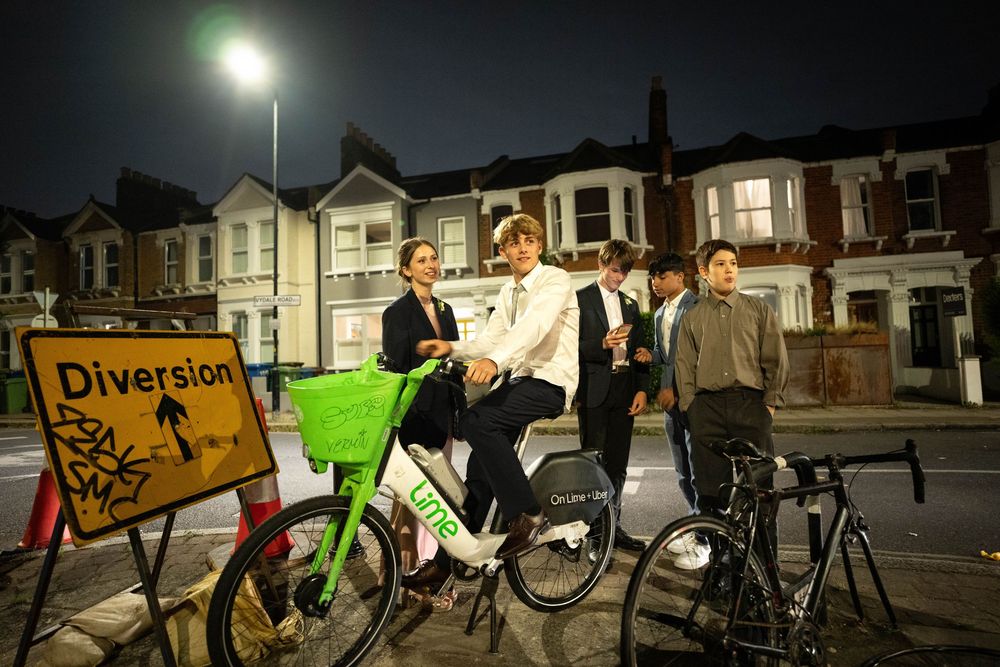 A group of cyclists gathered near a street diversion sign at night under a streetlight on a residential road.