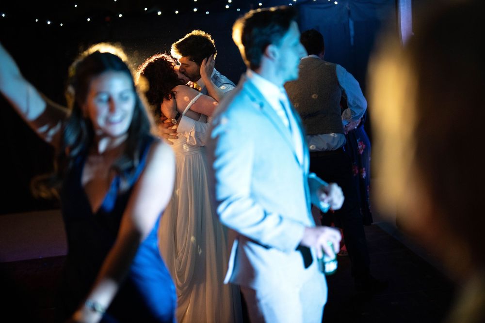 People dancing at a dimly lit party with a person in white suit and others in formal attire on the dance floor.