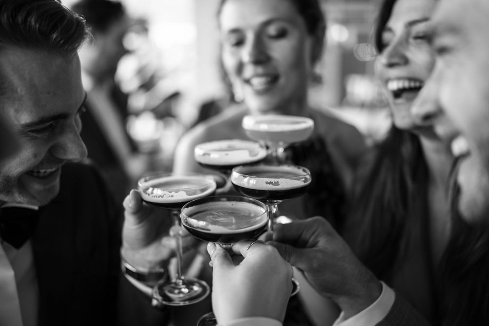 Friends toasting and laughing together with cocktail glasses in black and white photography.