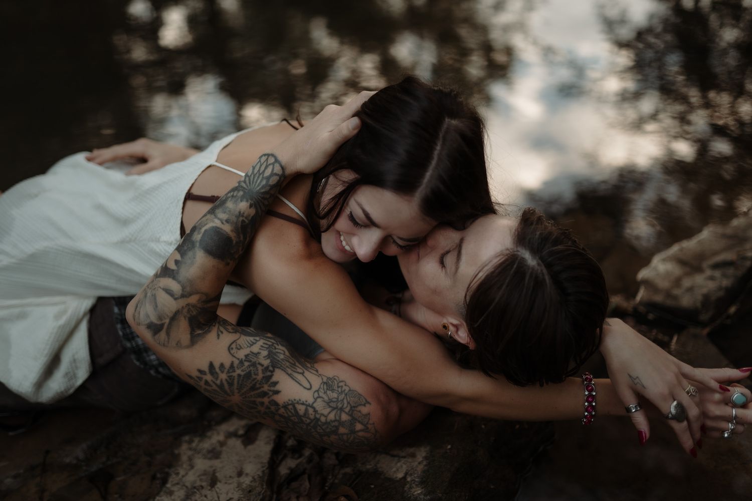 Two people share an intimate embrace outdoors in moody lighting.