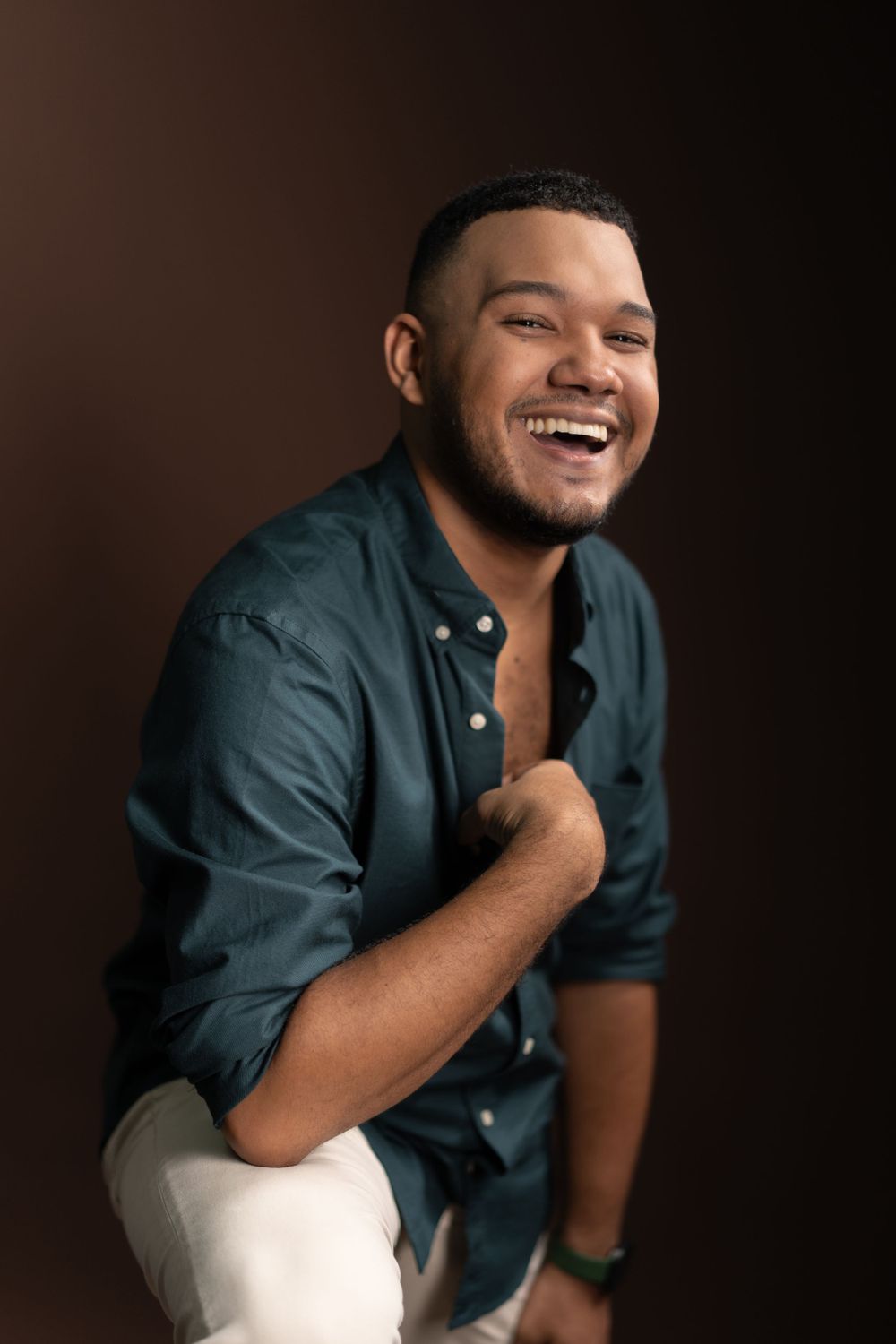 Studio portrait of person in blue button-down shirt laughing against brown background.