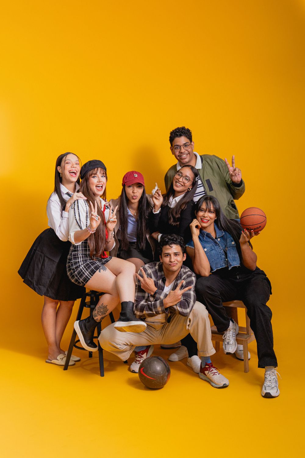 Group of friends pose playfully with basketball against bright yellow background.