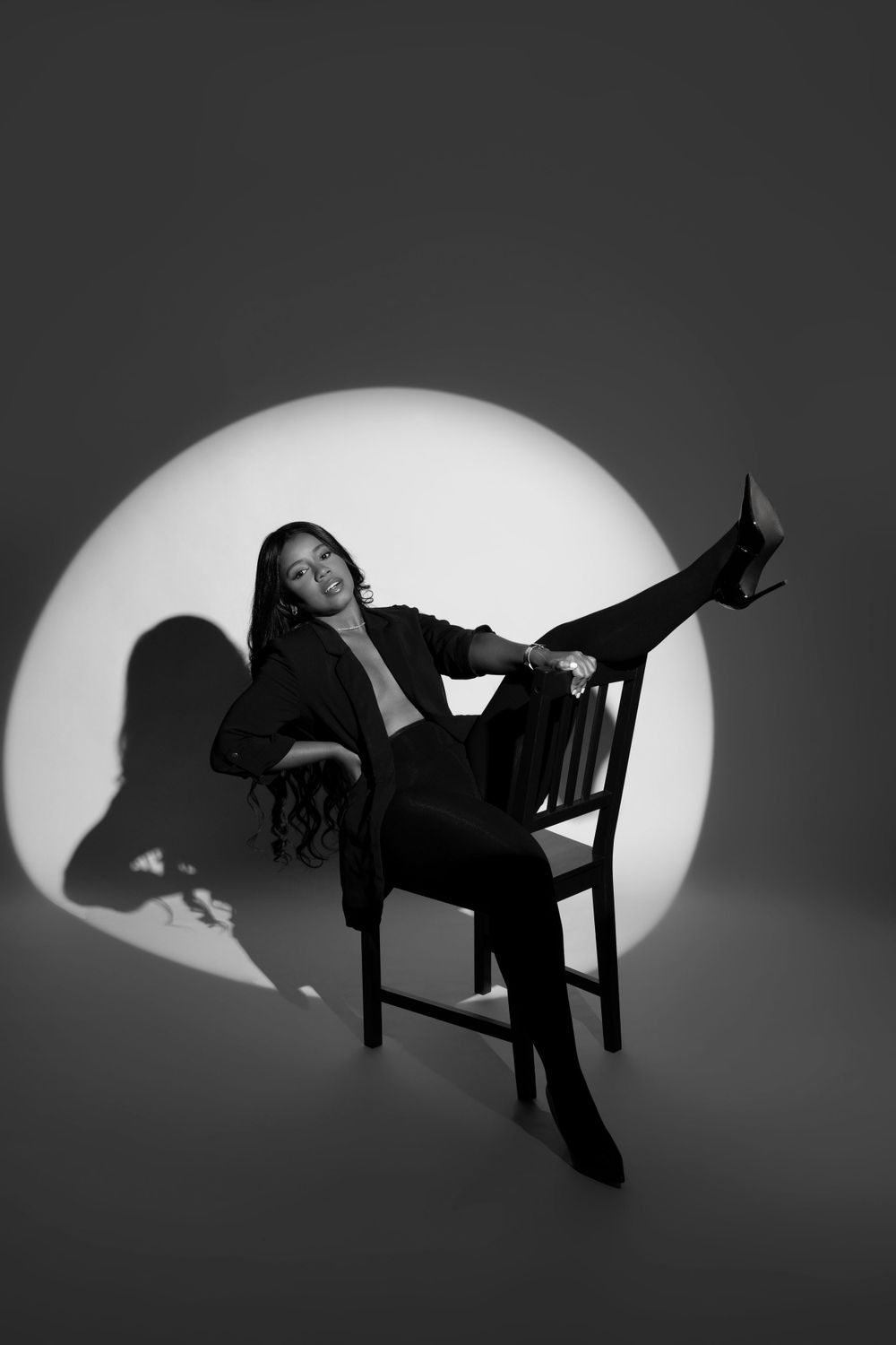 Dramatic black and white portrait with figure lounging on chair against circular spotlight.