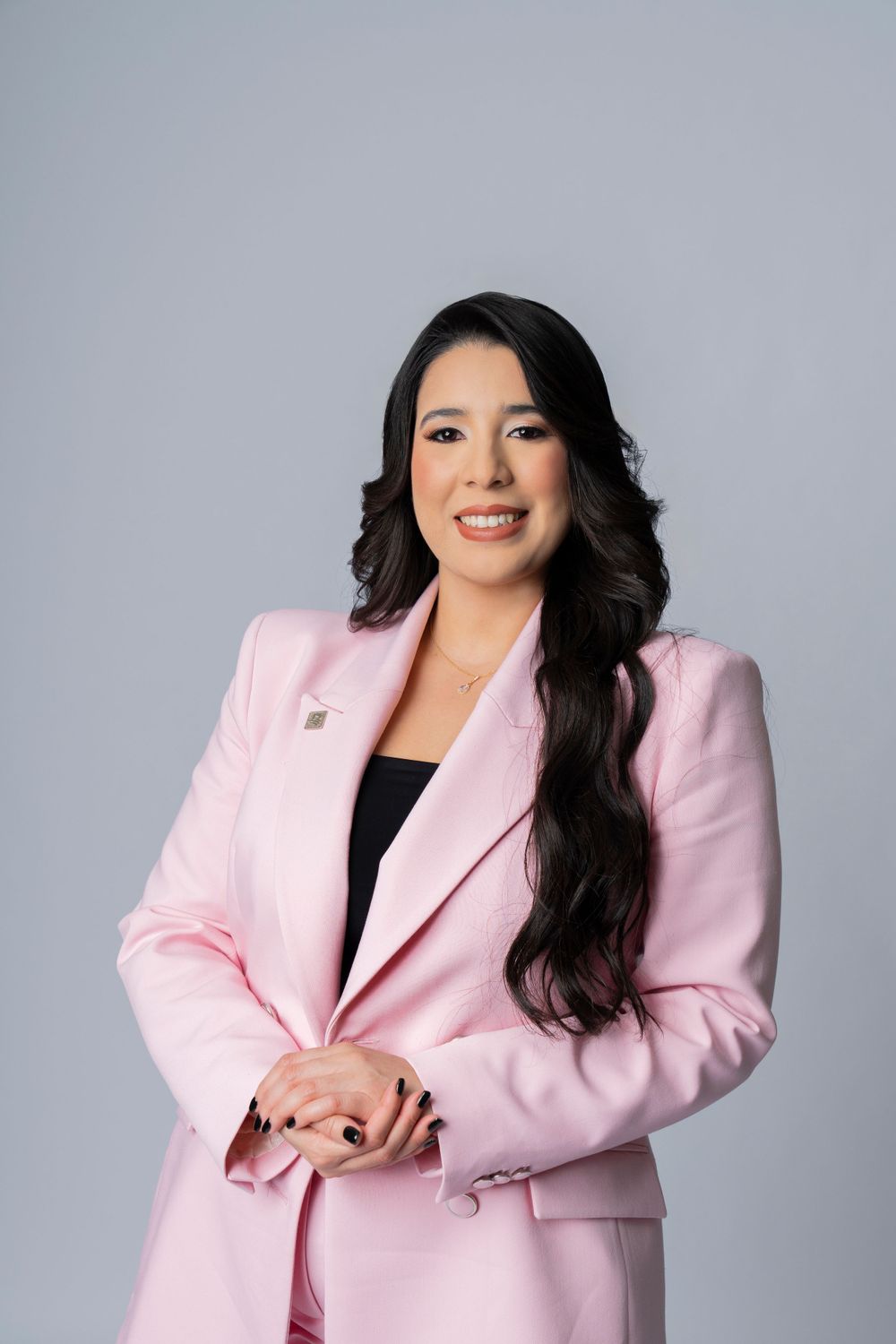 Professional headshot of woman wearing pink blazer against grey background.
