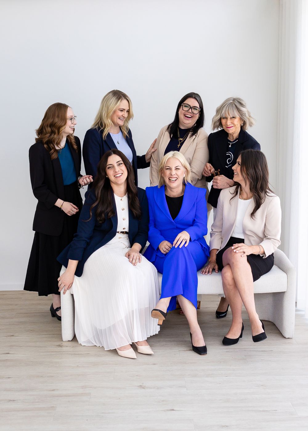 Group of people in coordinated business outfits sitting together against a white studio backdrop.