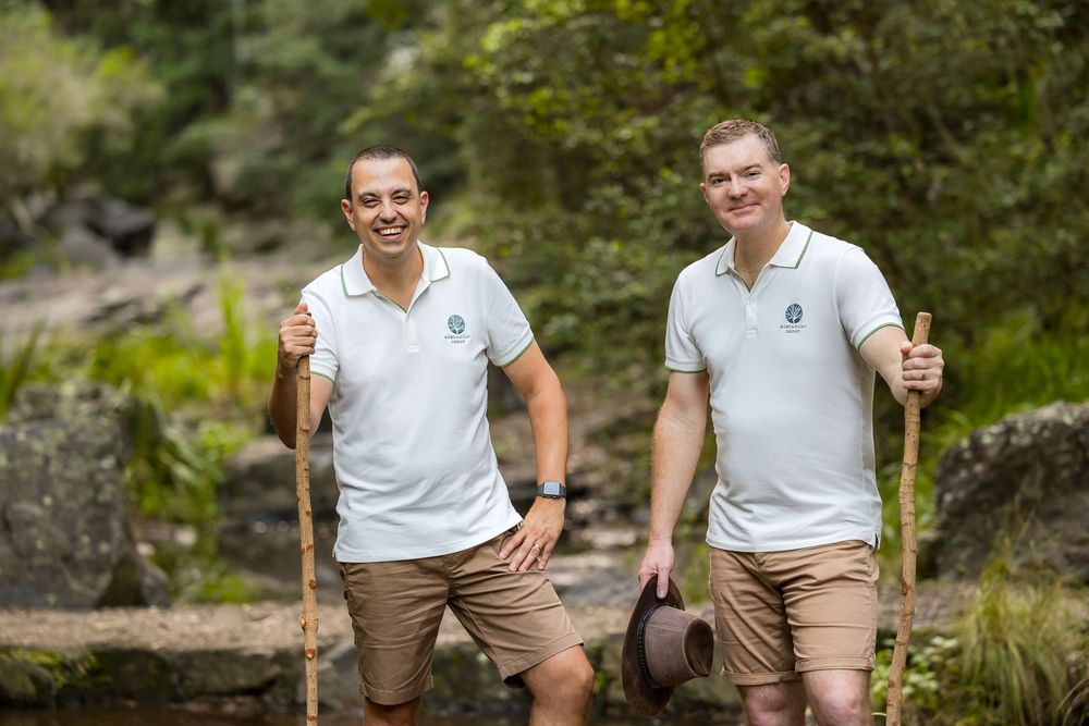 Students in school uniforms sit and smile on stone steps in an outdoor garden setting.