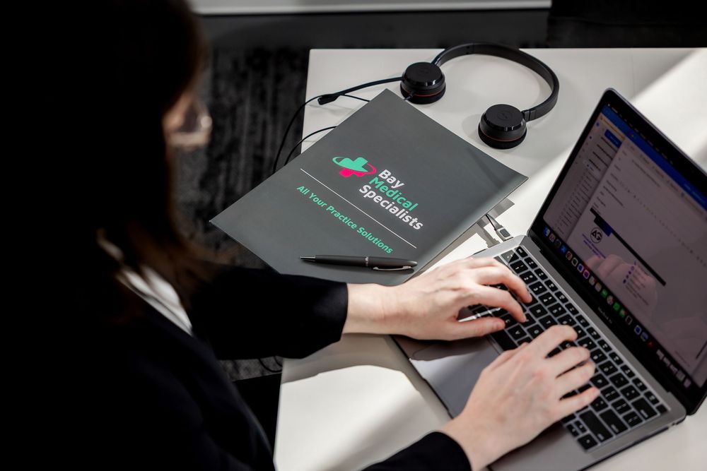 Close-up view of hands typing on a laptop keyboard with multiple screens in dark office setting.