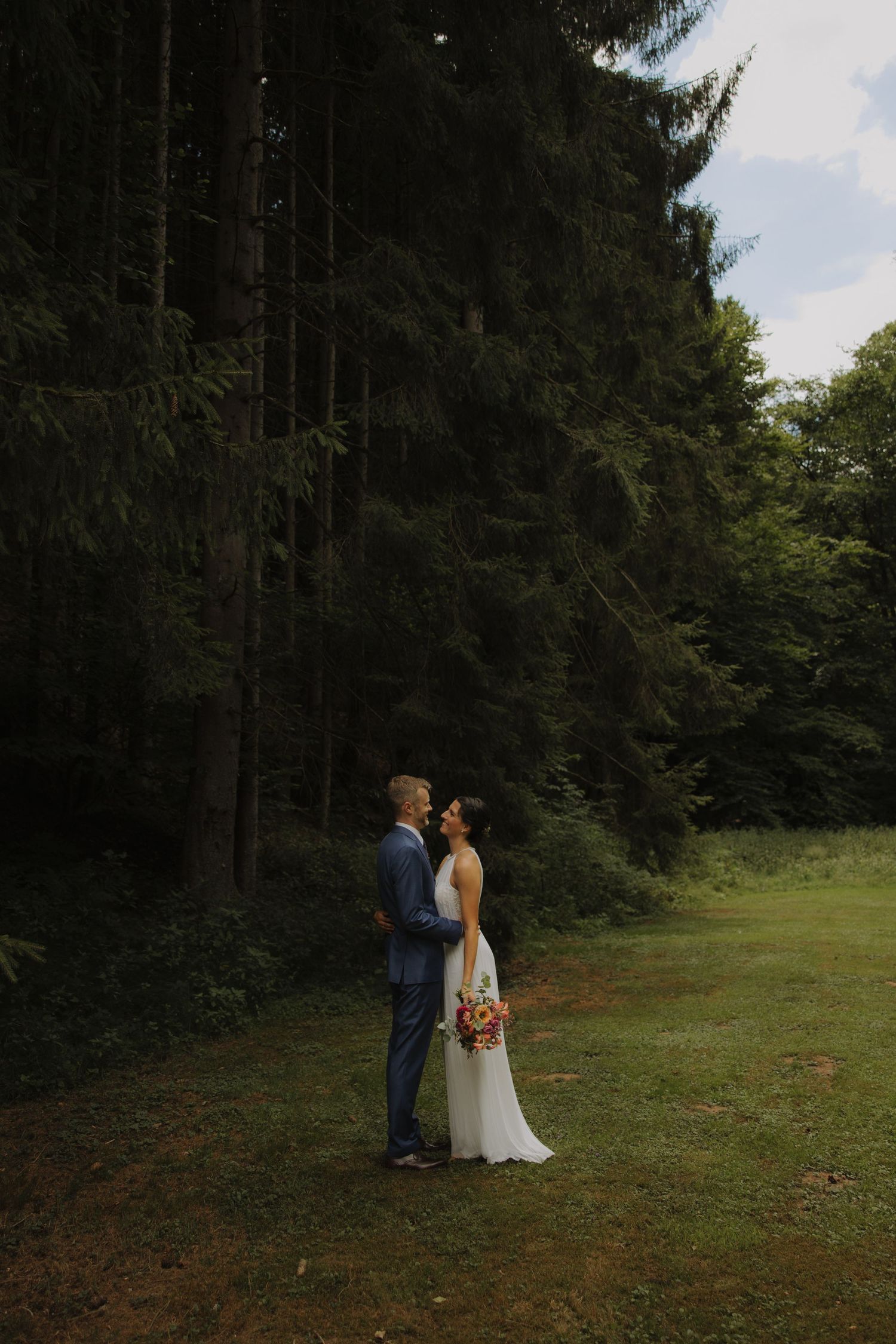 Romantic couple in wedding attire sharing intimate moment against natural backdrop.