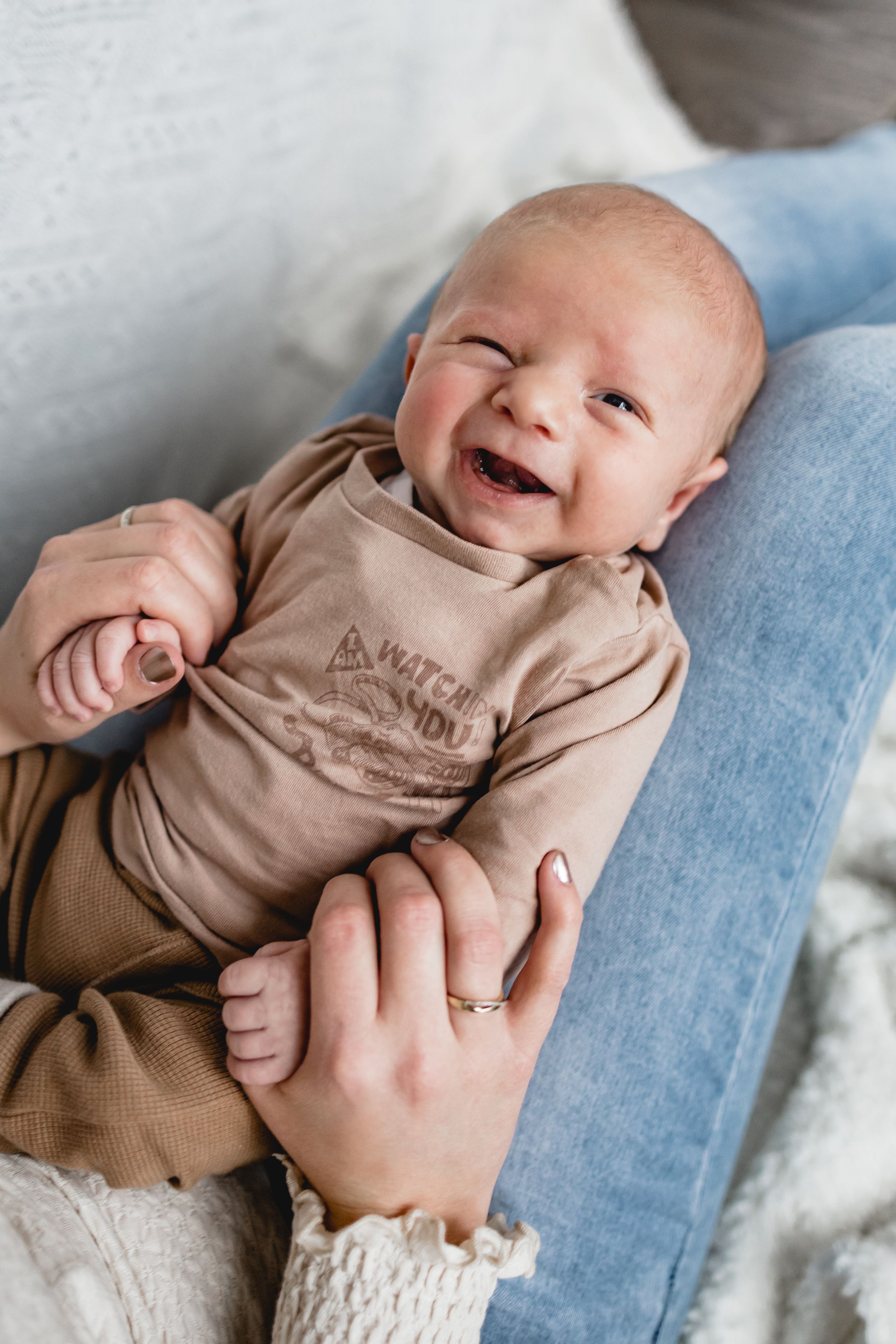 Happy baby in brown onesie smiling while lying on blue surface.