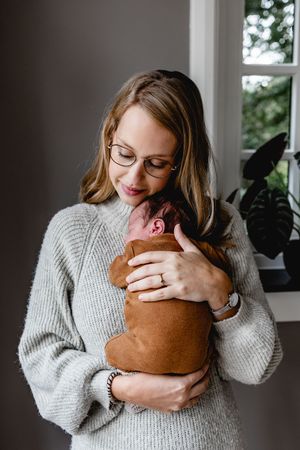 Person in grey sweater cuddling with brown dachshund by window.