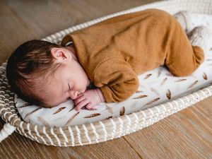 Sleeping newborn in brown sweater on textured white blanket.