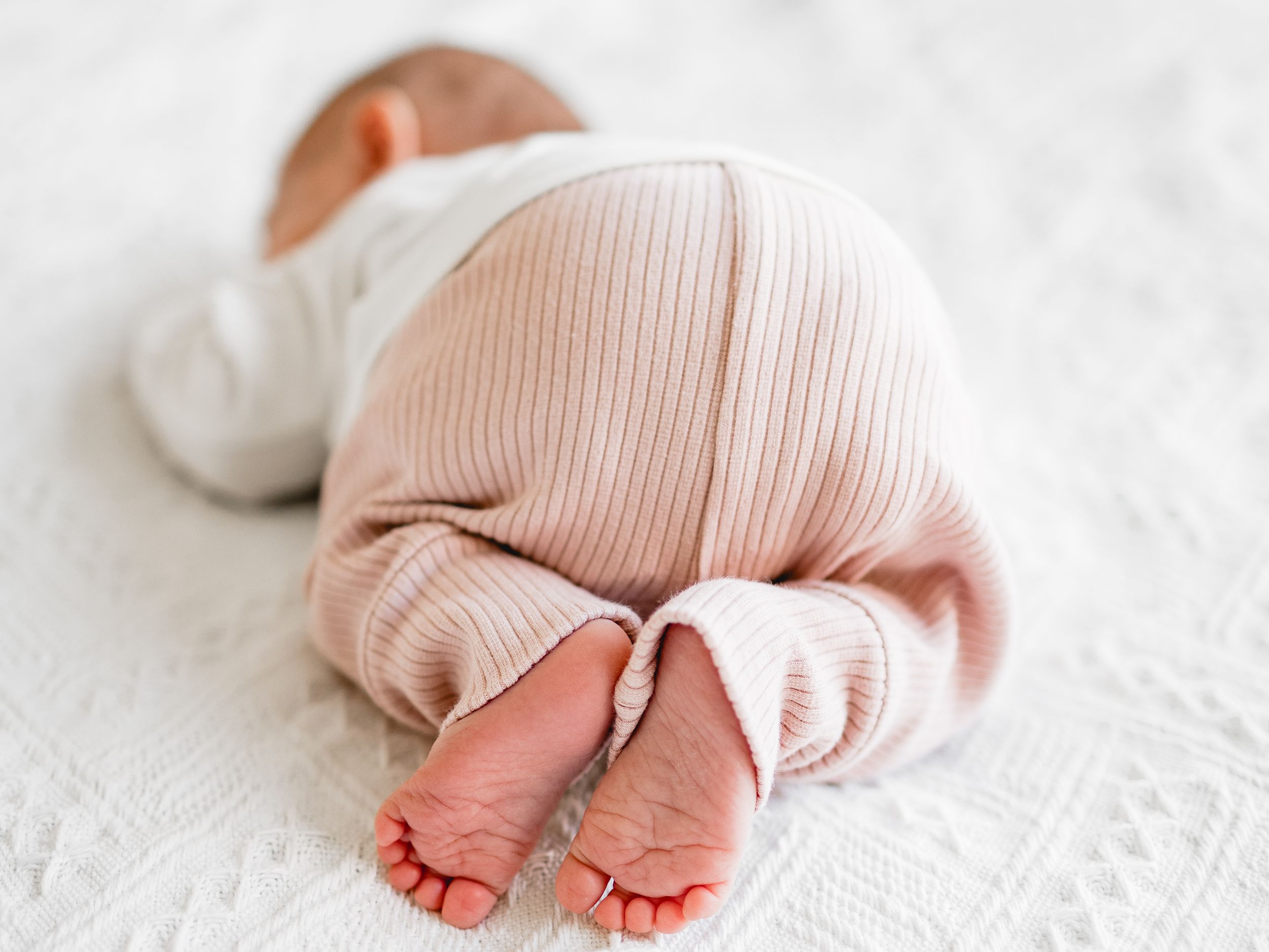 Tiny baby feet in pink knit clothing against white textured background.