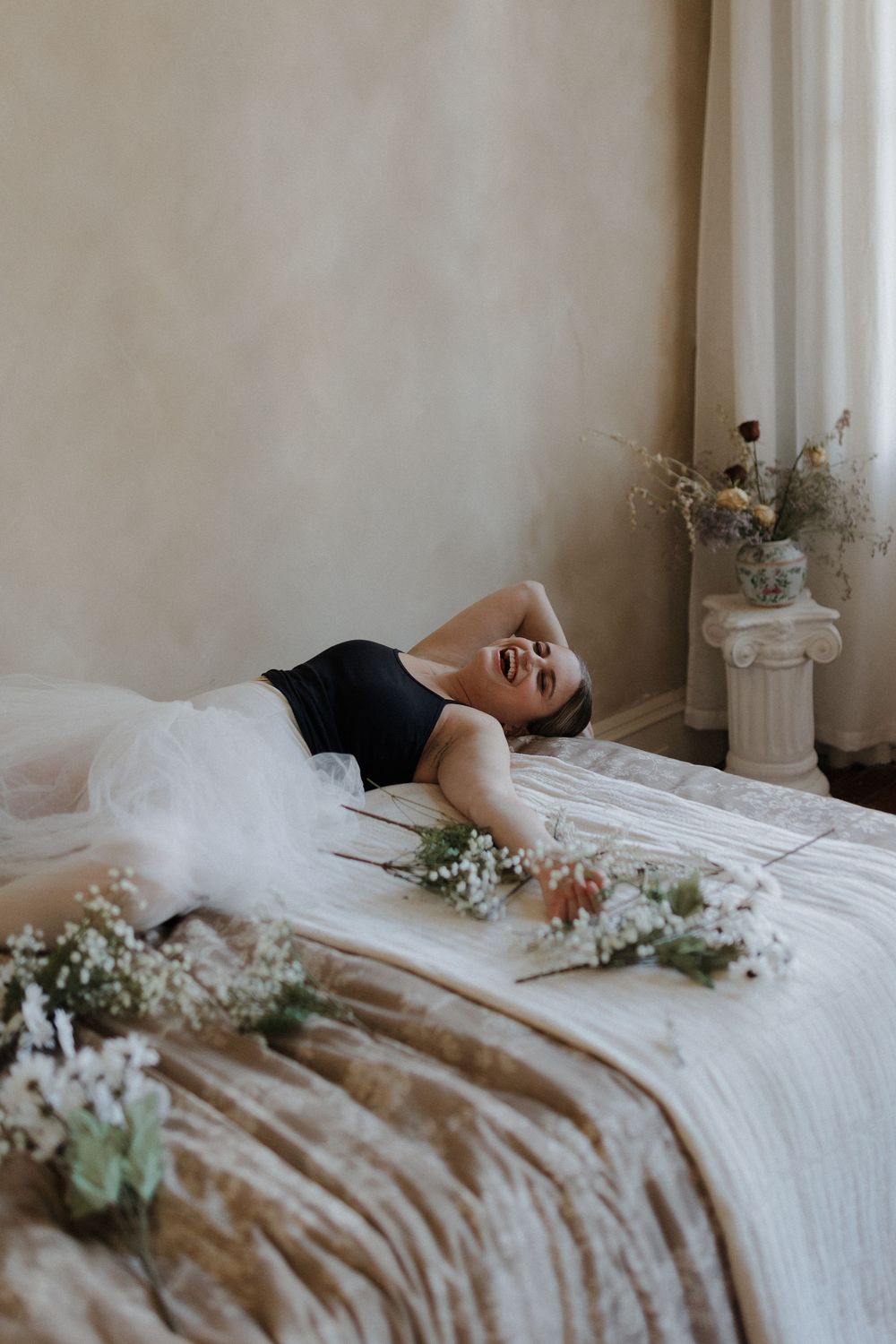 Dancer in black bodysuit and tulle skirt laughing while lying on bed.