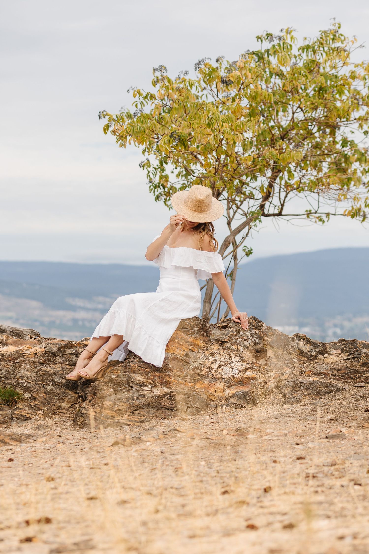 White dress flowing in the breeze against a scenic mountain backdrop on a sunny afternoon.