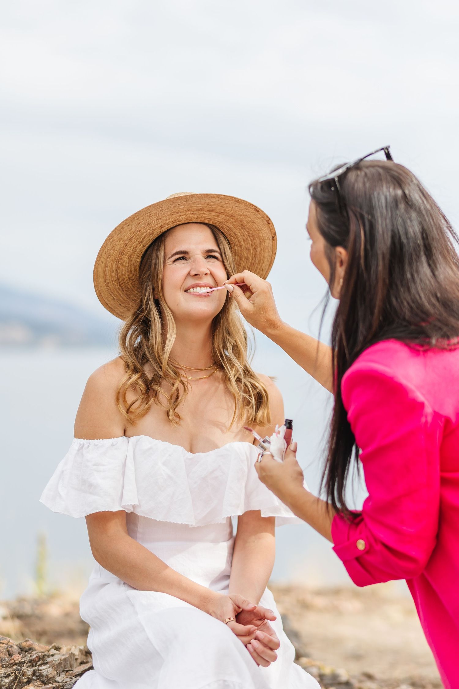 Two people in a sunny outdoor setting, one wearing a white dress and straw hat, sharing a joyful moment together.