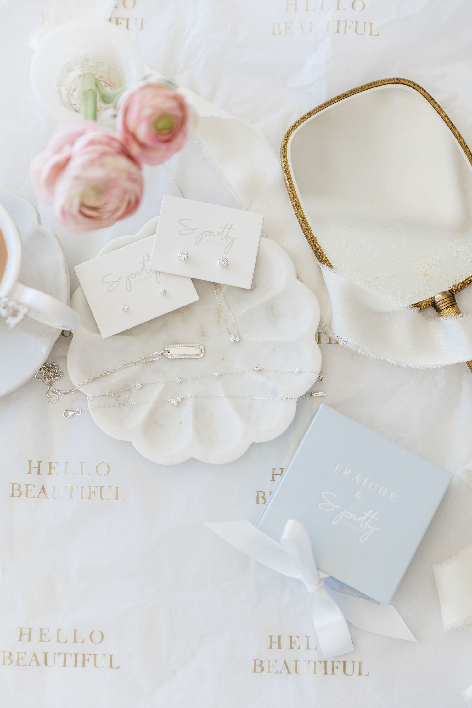 Elegant jewelry flatlay with pearl earrings, necklace, mirror, pink roses, and Hello Beautiful gift wrap.