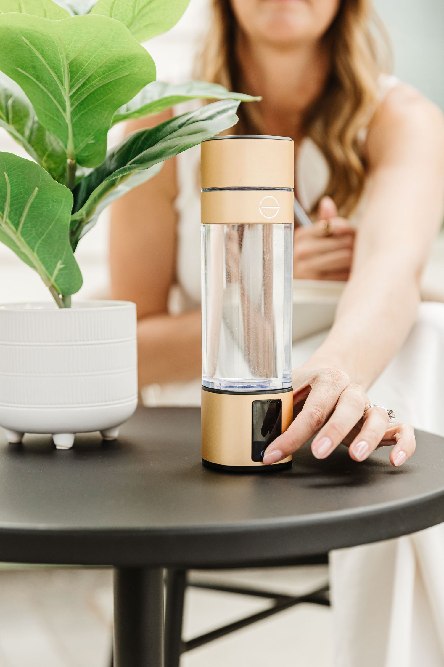 White ceramic planter with fiddle leaf fig plant on black table with glass container.