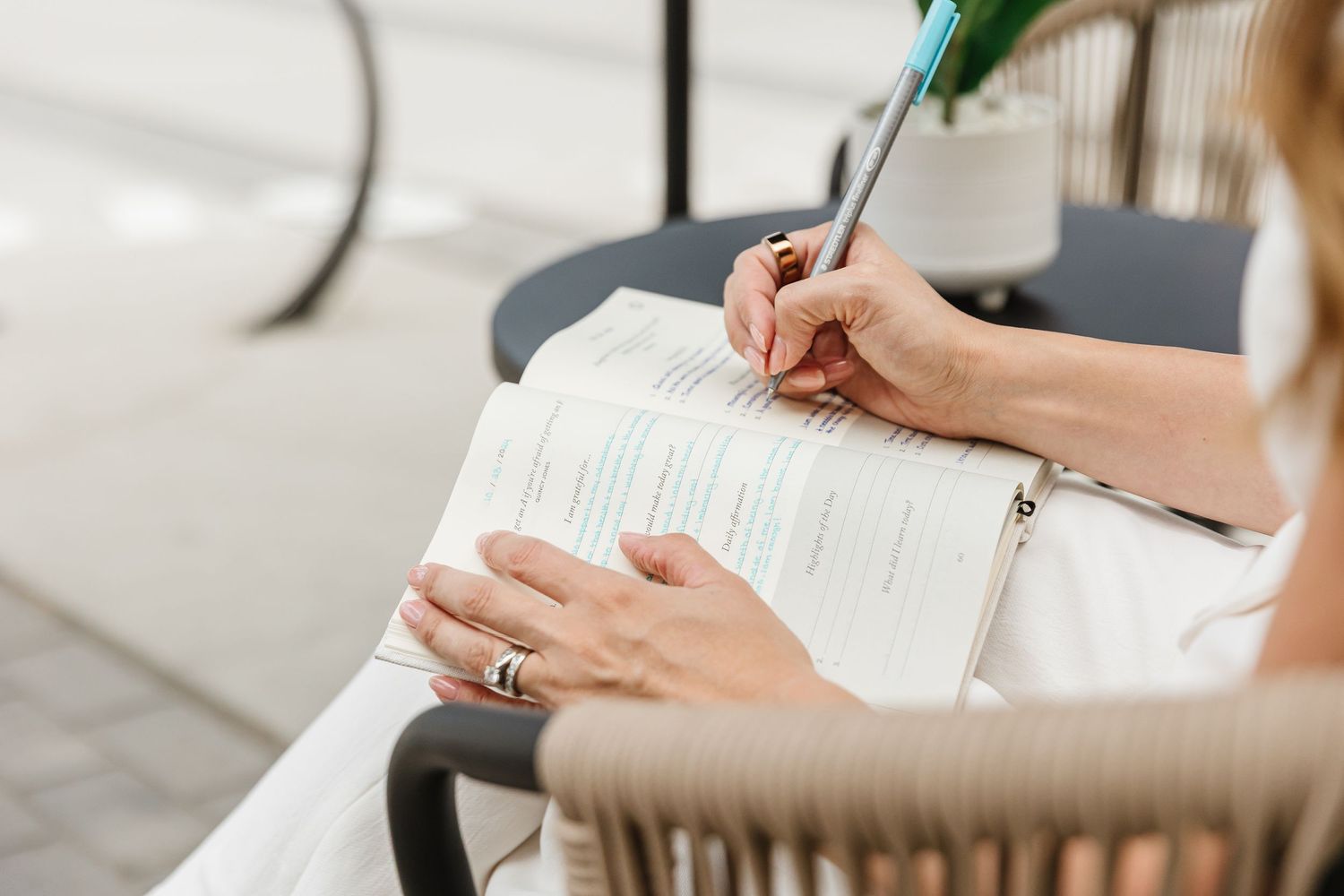 Close up of hands writing in notebook on white surface with natural lighting.