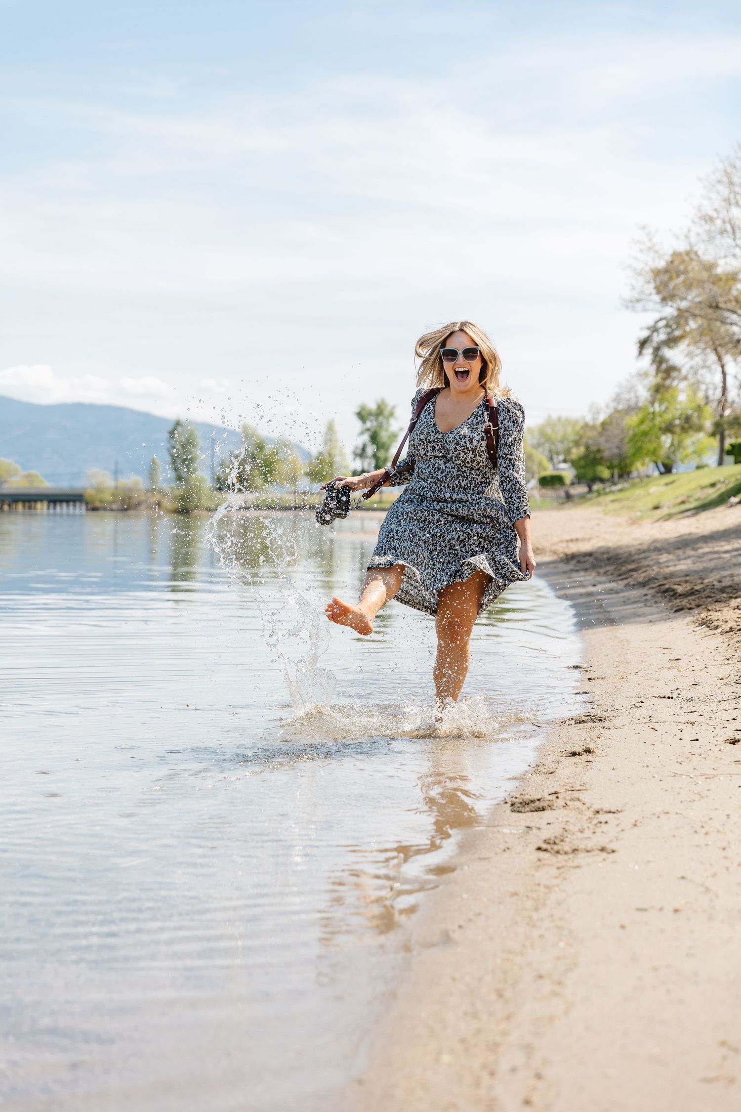 A woman in a polka dot dress splashes playfully in the shallow waters of a lake on a sunny summer day.