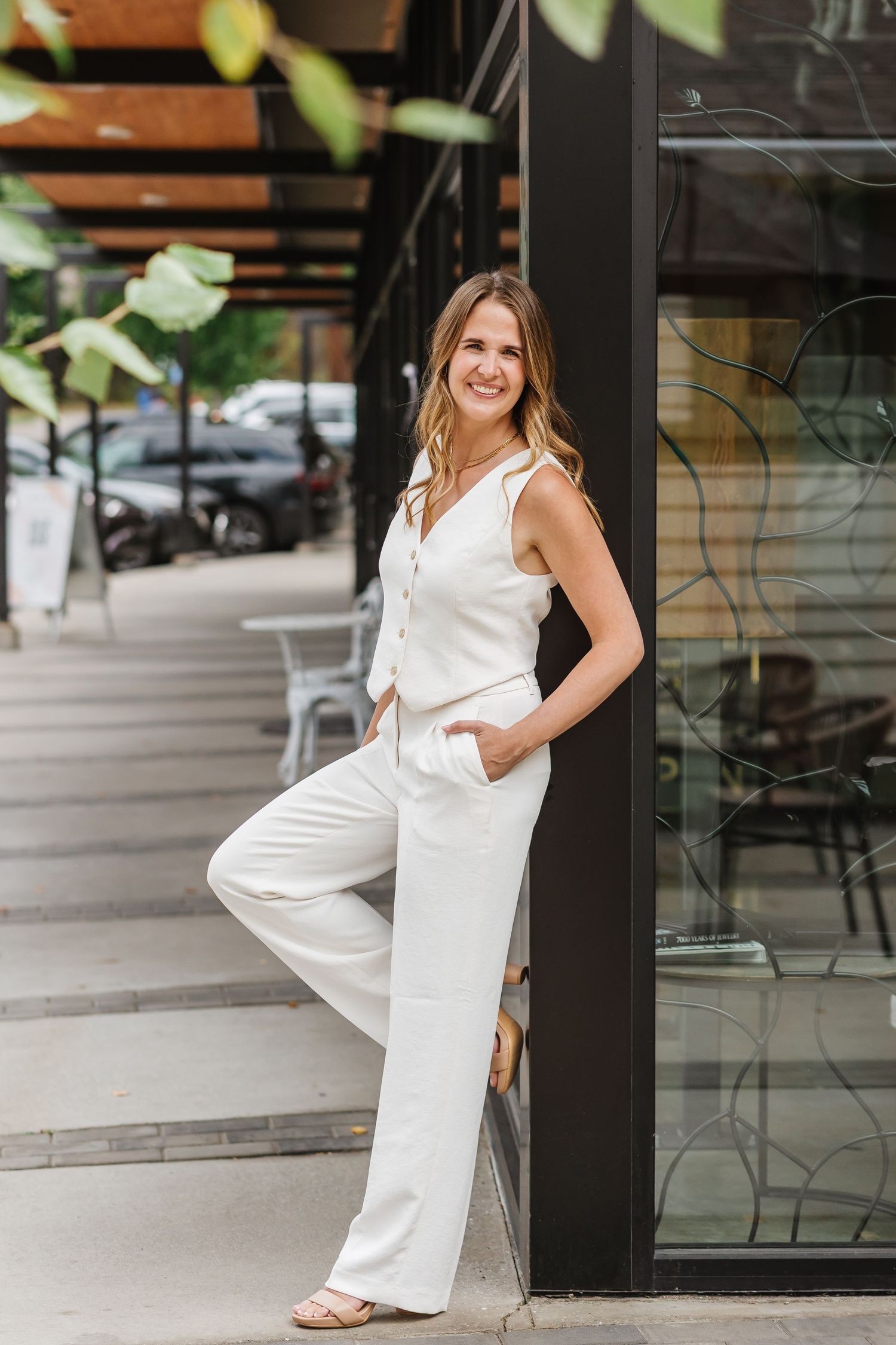 Person wearing crisp white outfit poses confidently against modern storefront with glass and metal details.