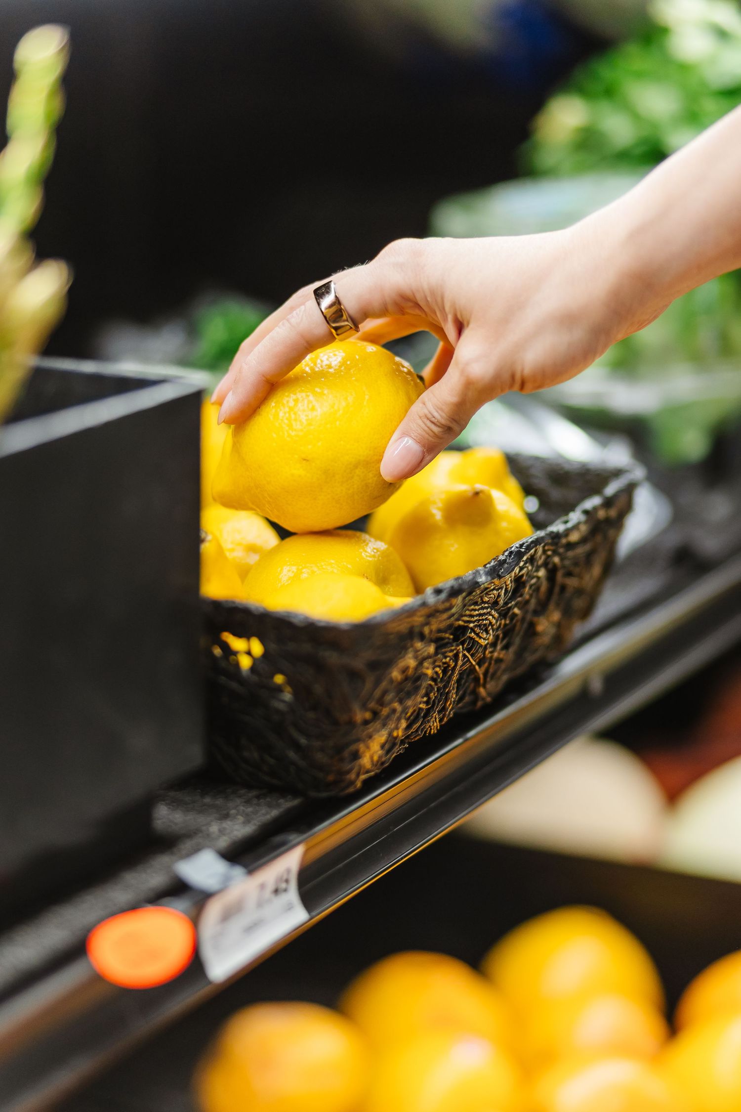 Fresh citrus fruits being placed into a dark decorative bowl against a blurred background.